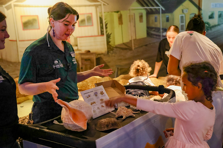 A Wonders of Wildlife volunteer stands behind a table of sea shell samples and speaks to guests.