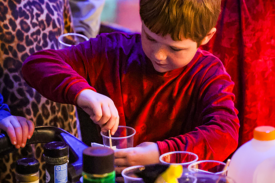 A young boy mixes paint in a plastic cup.