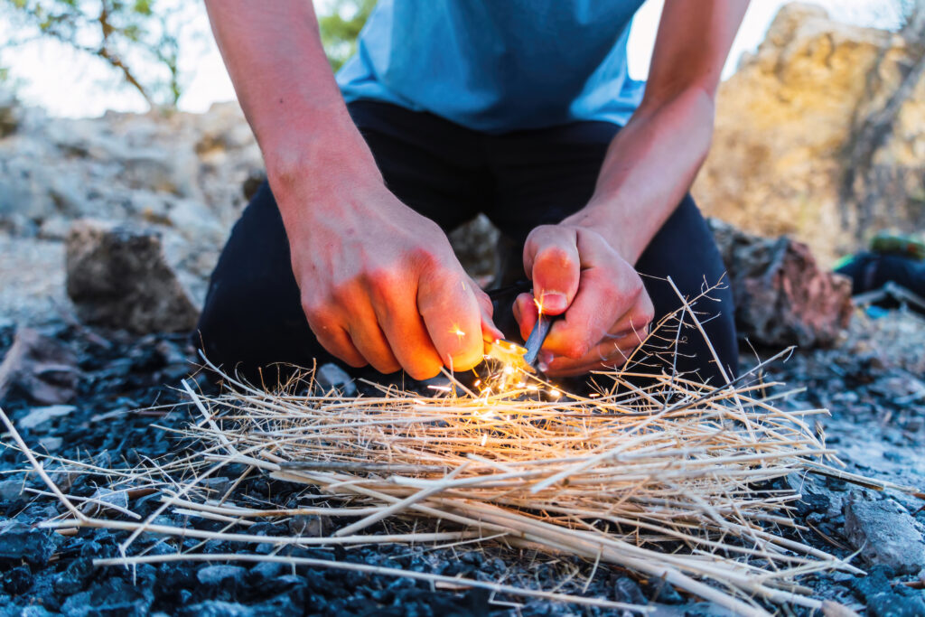 Close up view of a young male starting a fire with flint and steel outside. Survival concept.