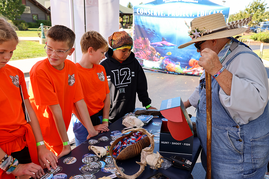 A volunteer interacts with some students admiring a collection of artifacts on a table.