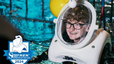A young boy wearing glasses smiles through his dive helmet as he wades in the shake dive tank at Wonders of Wildlife.