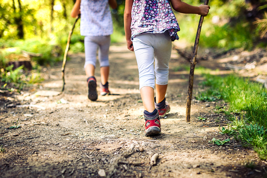 Two people hiking down a wooded trail with walking sticks.