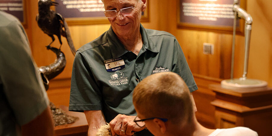 A WOW volunteer smiles as a guest interacts with an animal pelt experience.